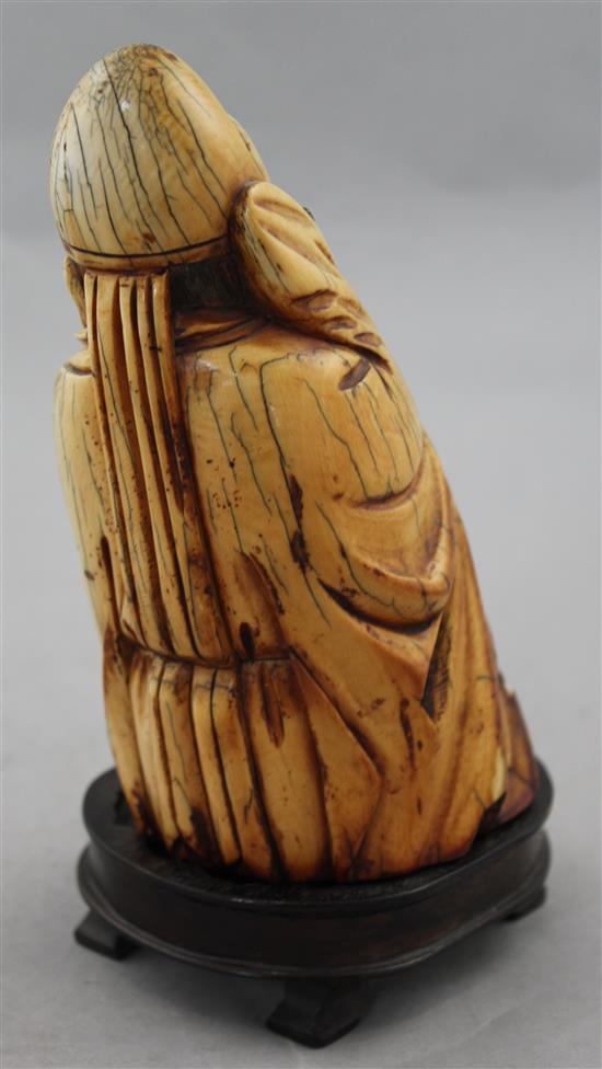 A Chinese mammoth ivory carving of a seated figure of Li Bai, holding a book, 16.5cm, wood stand